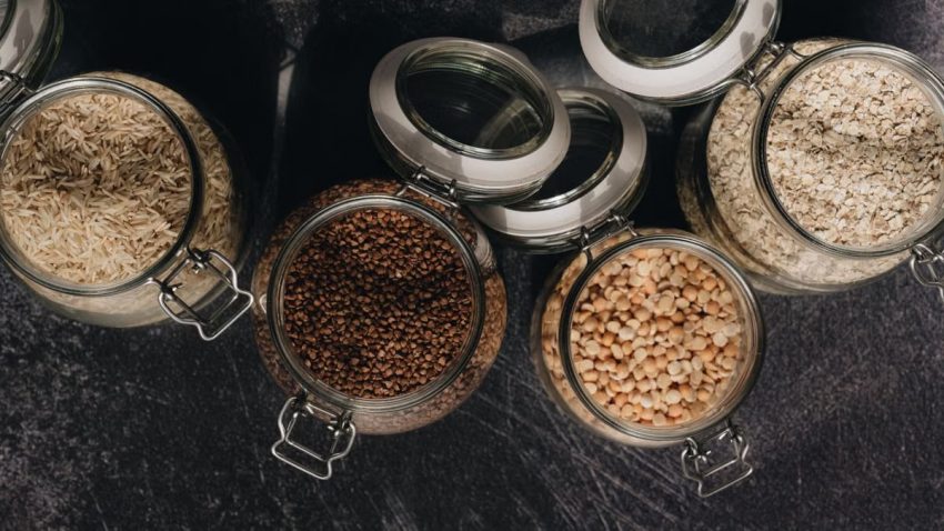 Aerial shot of diverse grains in glass jars showcasing buckwheat, rice, oats, and pulses.