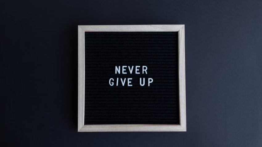 Inspirational letter board with 'Never Give Up' phrase on gray background.